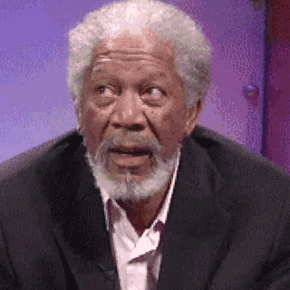 a man with a beard is wearing a suit and a pink shirt and making a surprised face .