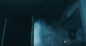 a man is holding a gun in a dark room while another man stands behind him .