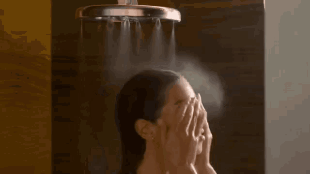 a woman is taking a shower with a shower head and washing her hair .