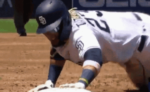 a baseball player wearing a helmet and gloves is crawling towards the base .
