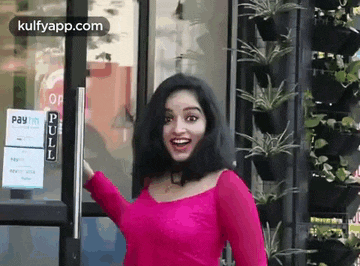 a woman in a pink dress is standing in front of a glass door .