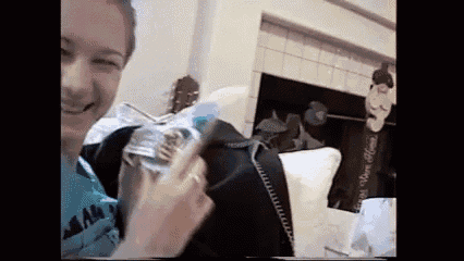 a woman is holding a bottle of water and smiling while sitting in front of a fireplace .