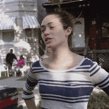 a woman in a blue and white striped shirt stands in front of a red ford car