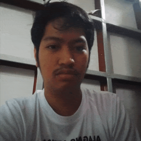 a man wearing a white t-shirt with the word raja on it looks at the camera