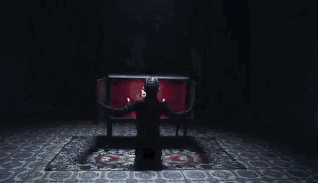 a man in a black robe is standing in front of a red coffin in a dark room .