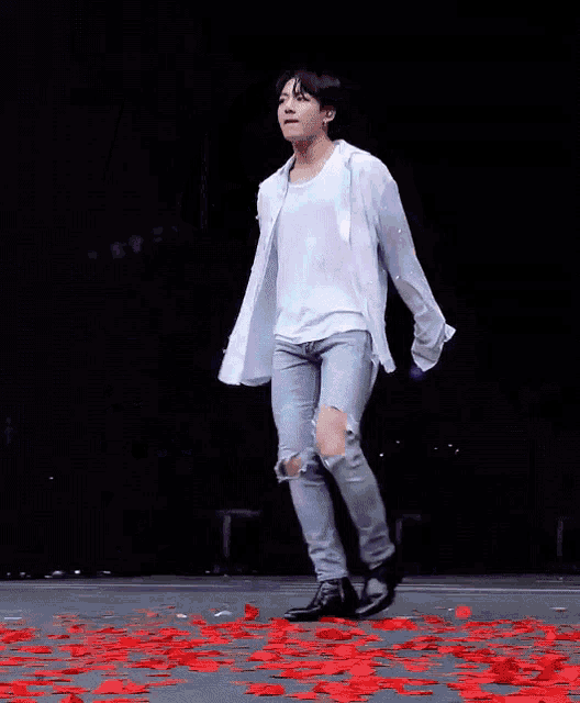 a man in a white shirt and ripped jeans is holding a microphone while dancing on a stage .