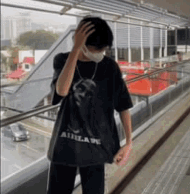 a man wearing a mask and a black t-shirt is standing on a balcony .