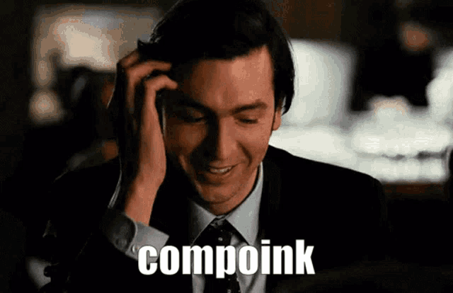 a man in a suit and tie is talking on a cell phone and the word compoink is on the screen
