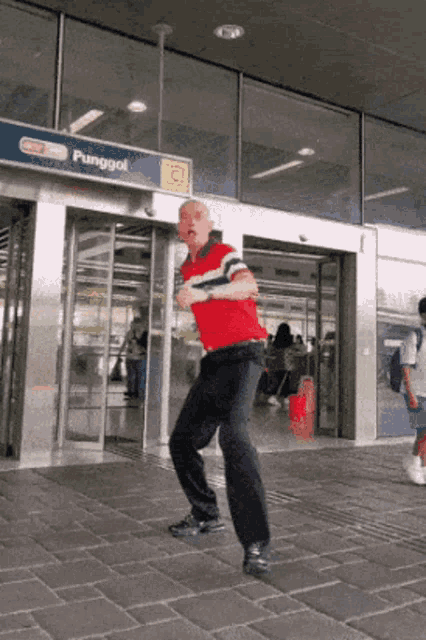 a man in a red shirt is dancing in front of a sign that says punggol