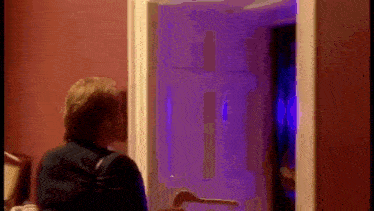 a woman is standing in front of a door with a purple light shining on it .