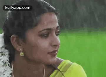 a close up of a woman 's face in the rain wearing a yellow saree and earrings .