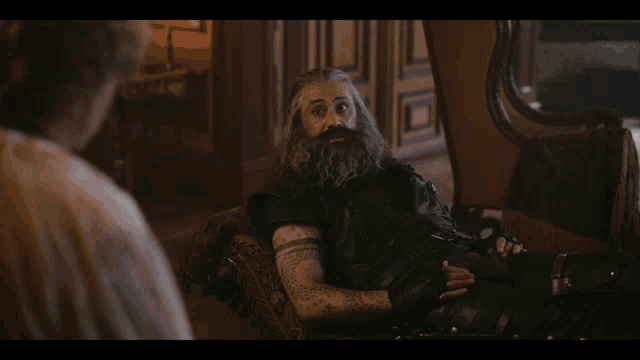 a man with a beard is sitting in a chair with the words you 're a fuckin lunatic and i like