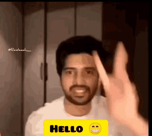 a man with a beard waves his hand in front of a yellow hello sign