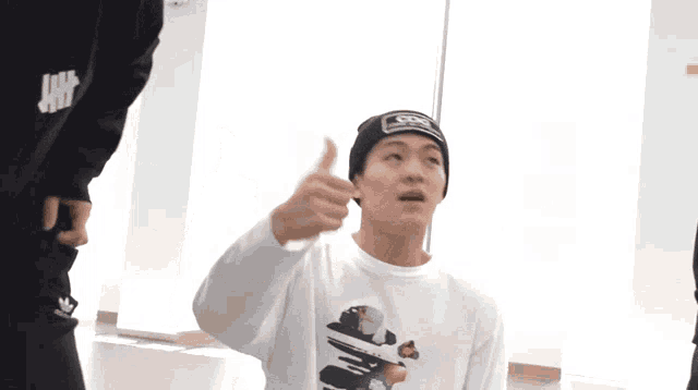 a man wearing a white shirt and a black hat with the letter s on it gives a thumbs up