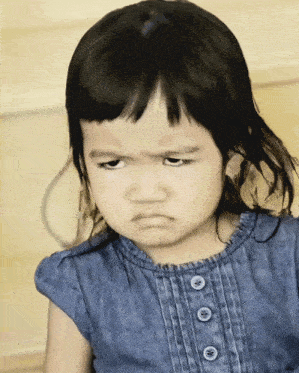 a little girl wearing a blue shirt with buttons on the front looks angry