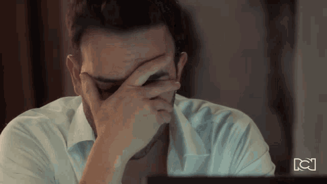 a man covering his face with his hand in front of a laptop screen