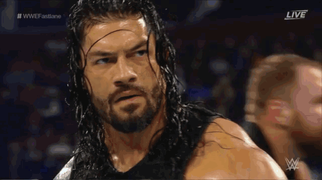 a man with long hair and a beard is standing in front of a screen that says wwe fastlane