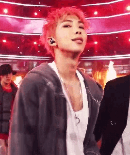 a man with pink hair is wearing a gray jacket and a white tank top .