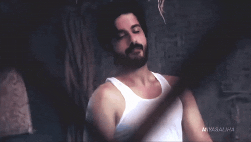 a man with a beard wearing a white tank top with the name miyasaliha at the bottom
