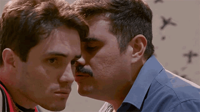 a man with a mustache kissing another man on the cheek
