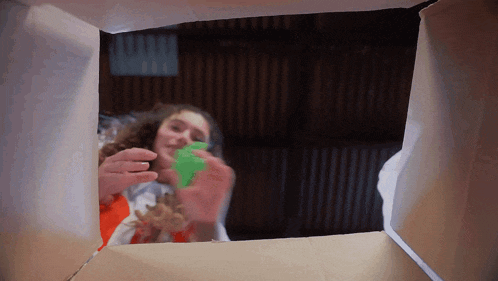 a girl is looking out of a cardboard box holding a green toy