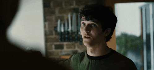 a young man in a green shirt stands in front of a brick wall with candles on it
