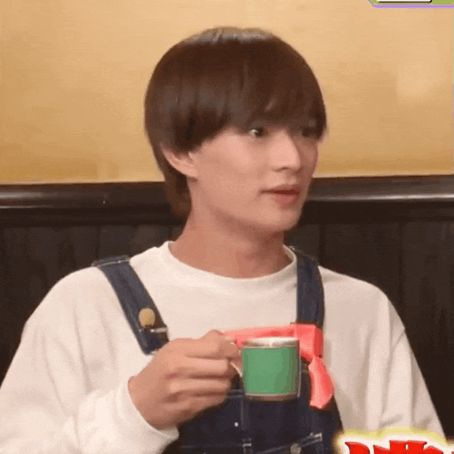 a young man wearing overalls is holding a cup of coffee