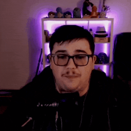 a man wearing glasses and headphones is sitting in front of a shelf with stuffed animals .