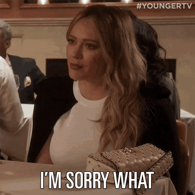 a woman is sitting at a table with a purse and says i 'm sorry what