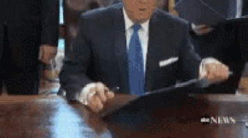a man in a suit and tie is sitting at a table holding a clipboard .