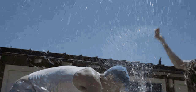 a man in a blue hat is being sprayed with water by another man .