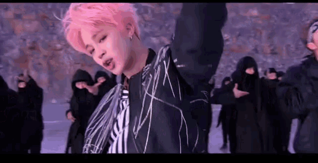 a man with pink hair is dancing in front of a group of people wearing masks .
