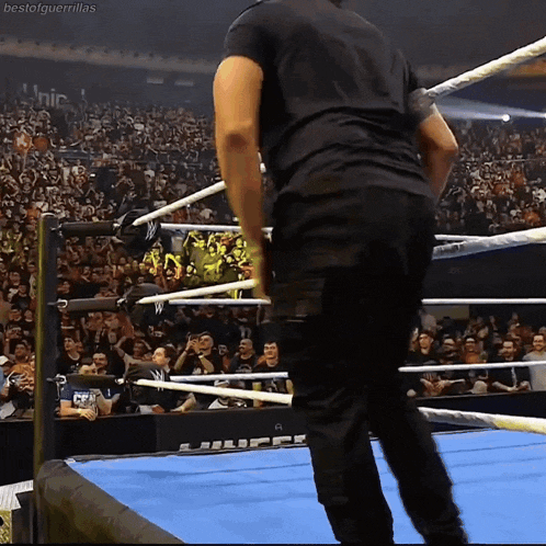 a man in a black shirt is standing in a wrestling ring with a crowd watching
