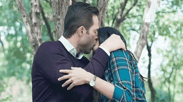 a man and a woman are kissing in front of a tree .