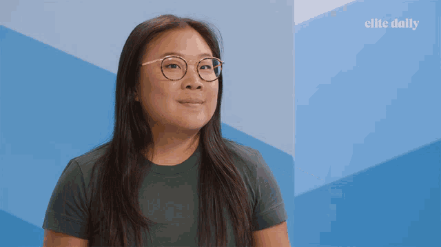 a woman wearing glasses is smiling in front of a blue wall that says elite daily on it