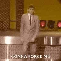 a man in a suit and tie is dancing on a stage with the words `` gonna force mb '' above him .