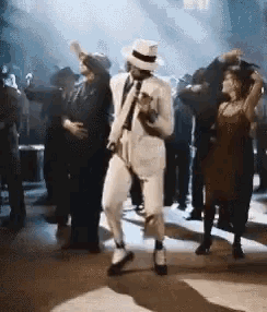a man in a white suit is dancing in front of a crowd .