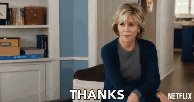a woman in a blue sweater is sitting in front of a sign that says thanks
