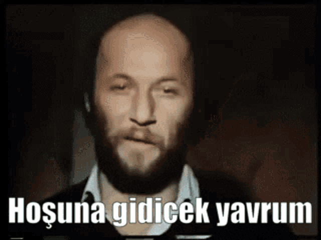 a bald man with a beard is looking at the camera with the words hosuna gidicek yavrum above him