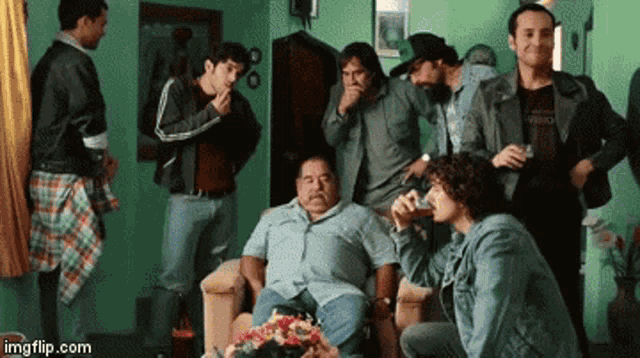 a group of men are gathered around a man sitting in a chair drinking from a glass