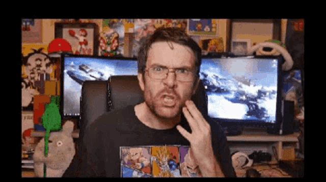 a man wearing glasses is sitting in front of two computer monitors