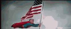 a man in a superman costume is flying in the air while holding an american flag .