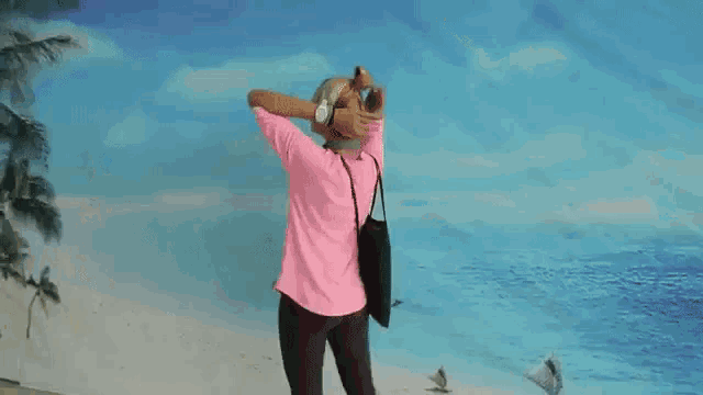 a woman in a pink shirt stands in front of a wall with a picture of a beach on it