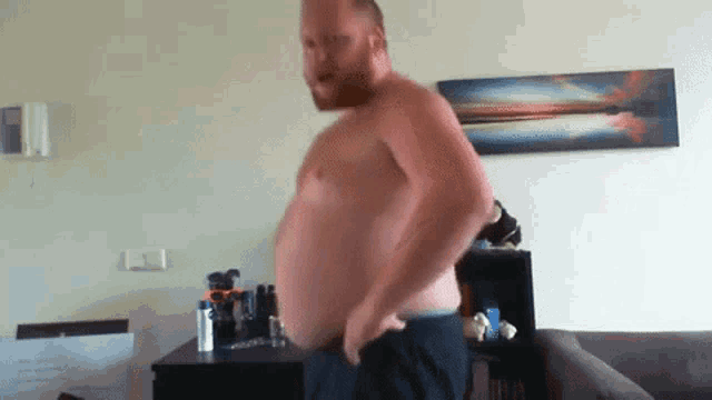 a shirtless man is standing in a living room with a painting on the wall behind him .