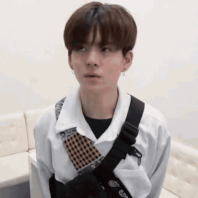 a young man wearing a white shirt and a black bag around his neck