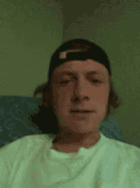 a man wearing a baseball cap and a white shirt is sitting on a couch .