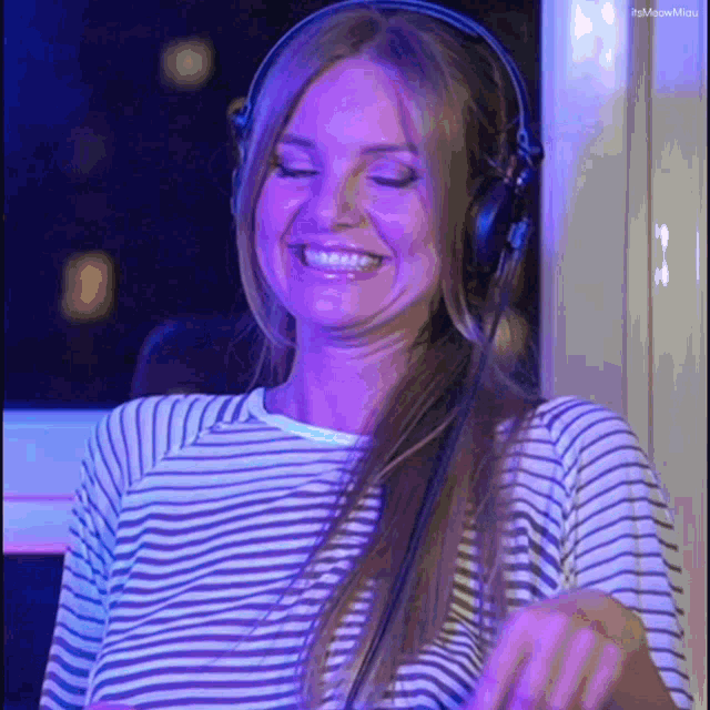 a woman wearing headphones and a striped shirt is smiling and dancing