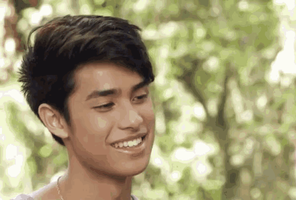 a close up of a young man 's face smiling in front of trees .
