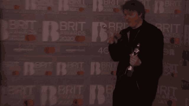 a man holding a trophy in front of a brit awards wall