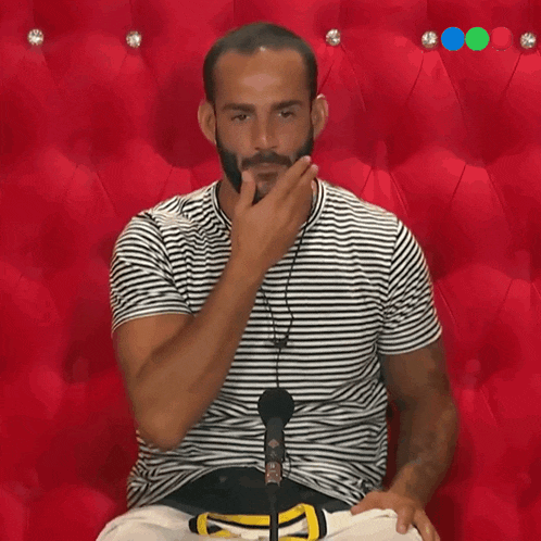a man in a striped shirt is sitting in front of a microphone and covering his mouth